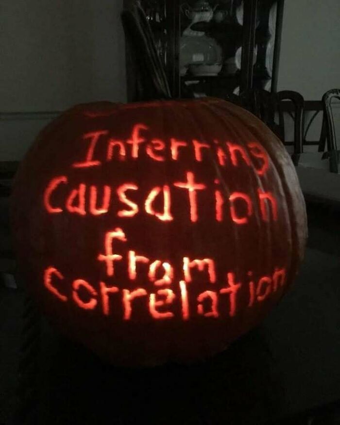 A carved pumpkin for Halloween with the words Inferring Causation From Correlation illuminated, a statistics meme.