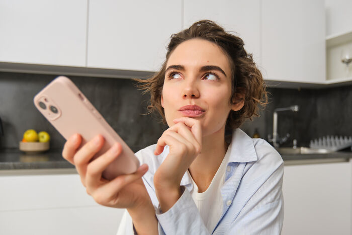 A thoughtful woman holding a smartphone, contemplating a sign from the universe and how to make real deals.