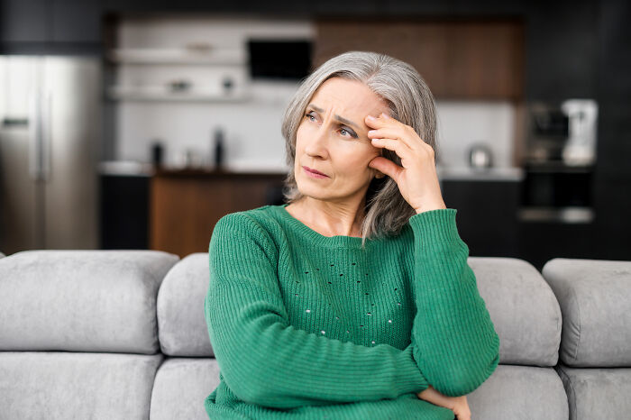 An older woman with a pensive expression, touching her forehead, reflecting on relationship red flags and mental health.