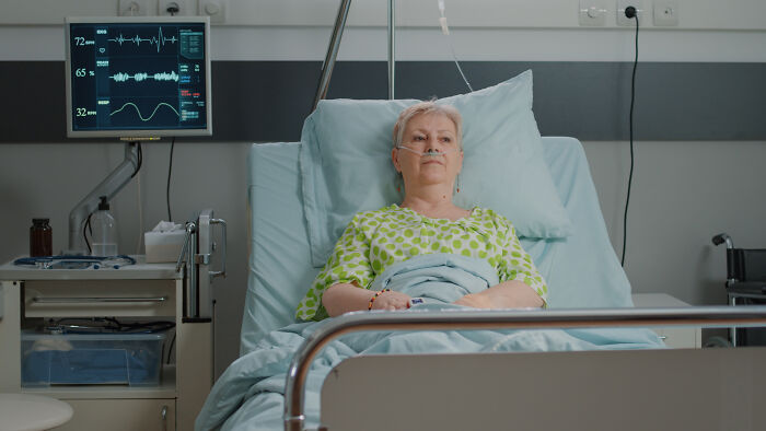 An elderly woman lies in a hospital bed, looking frail, a sign from the universe regarding health.