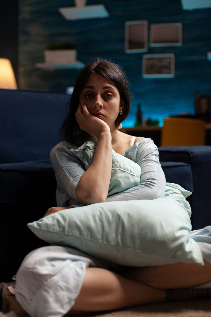 A distraught woman sitting on the floor with a pillow, contemplating if she's with the very wrong person.