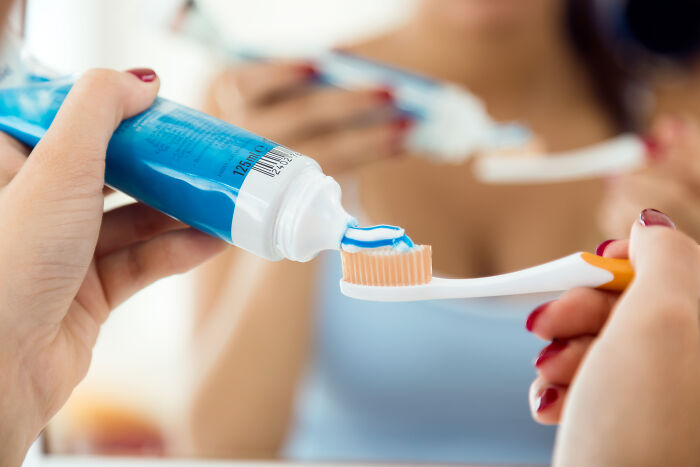 A person squeezing toothpaste onto a brush, illustrating a family house rule about bathroom etiquette.