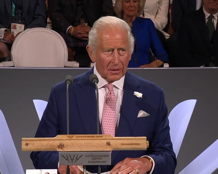 King Charles at a podium, speaking; Queen Camilla is visible in the background. Prince William and Kate Middleton.