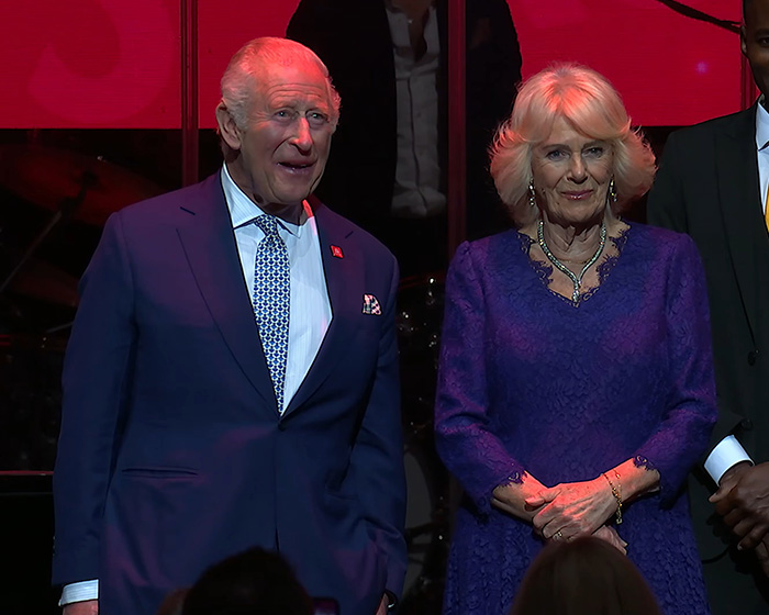 King Charles and Queen Camilla smiling at an event, reportedly demanding a name change.