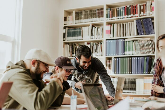 College life: Students laughing and working on laptops in a library, illustrating the complete freedom and new world of college.