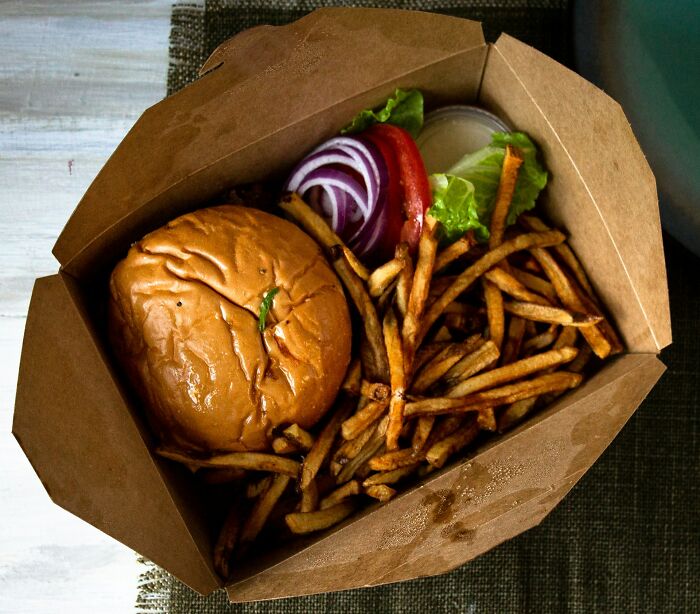 A delicious burger with fries and fresh vegetables in a takeaway box, highlighting poverty habits.