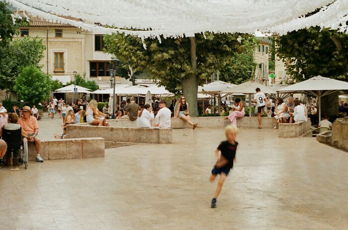 A blurry image of a child running in a town square with people sitting around, suggesting situations that scream horrible parent.