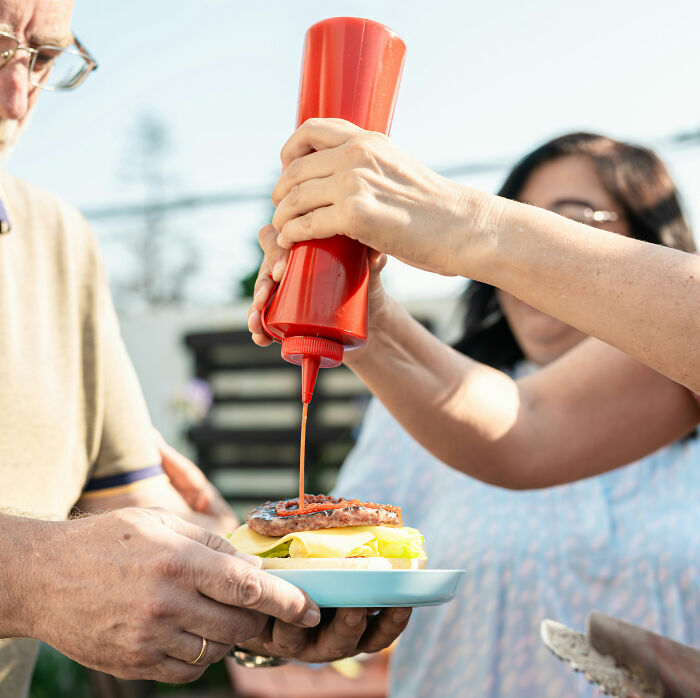 Hands squeezing ketchup onto a burger with cheese and lettuce, a simple act that could lead to unexpected riches.