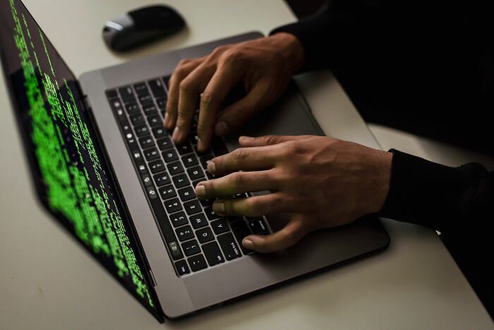 Hands typing on a laptop keyboard with green code on the screen, showing the random things people did that got them rich.