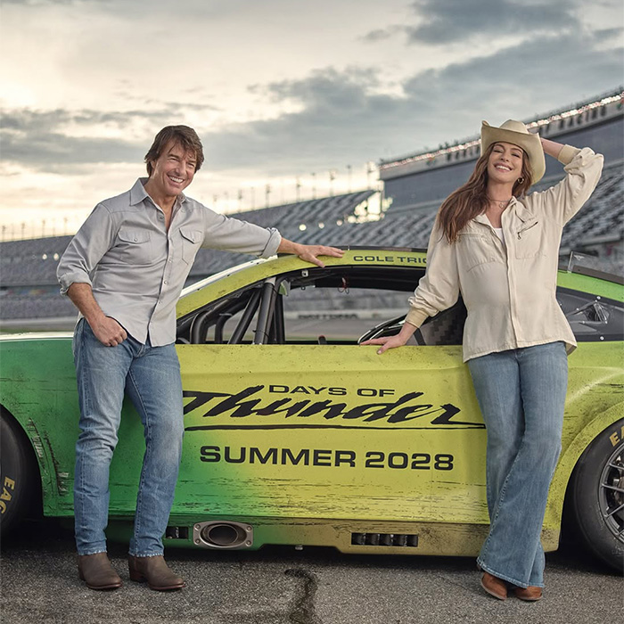 Tom Cruise and a woman with a cowboy hat posing next to a Days of Thunder race car. Tom Cruise and a woman with a cowboy hat posing next to a Days of Thunder race car.