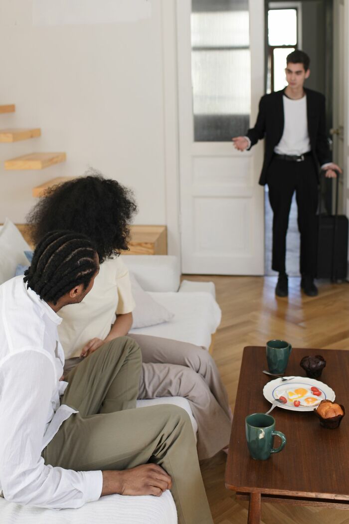 A man with a suitcase entering a room where two people are seated, illustrating friendships that fell apart.