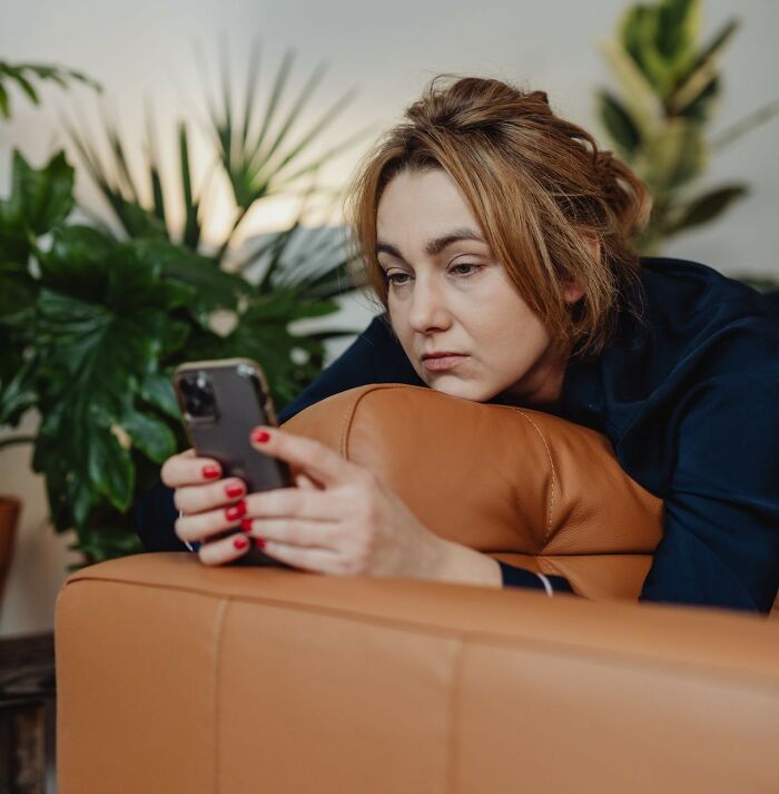 A woman on a couch looking at her phone, depicting the aftermath when friendships fall apart after years.