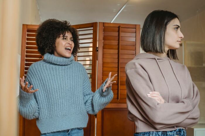 Two women in a room, one with curly hair gesturing animatedly, the other with arms crossed, showing friendships that fell apart.