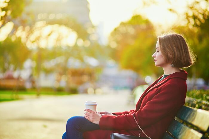 A woman sits on a bench in a park, eyes closed, reflecting on friendships that fell apart after years.