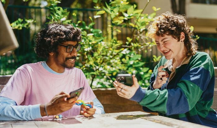 Two friends laughing while looking at phones, a friendship that might fall apart after years.