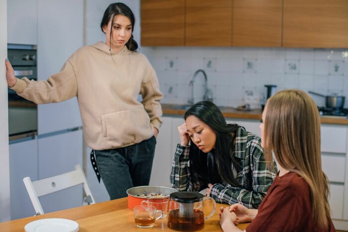 Three friends in a kitchen, two looking upset, representing friendships that fell apart after years.