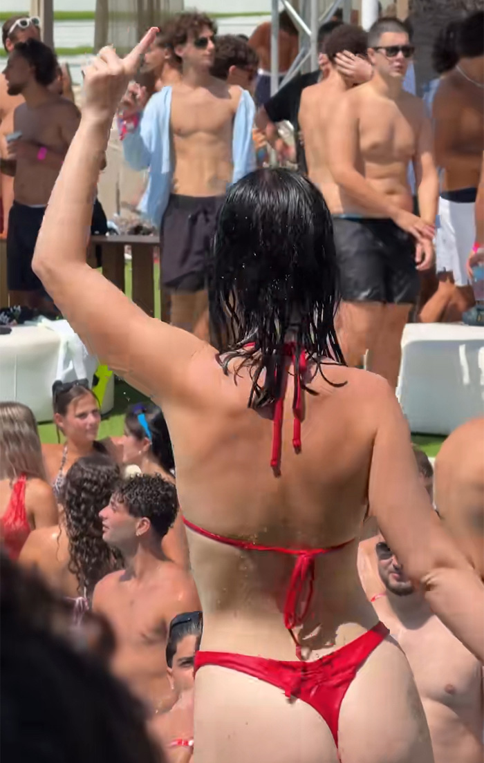 The viral red bikini girl in a red swimsuit, seen from behind, dancing at a lively outdoor pool party. The viral red bikini girl in a red swimsuit, seen from behind, dancing at a lively outdoor pool party.