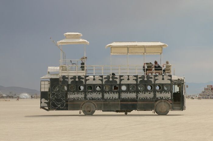 An elaborately customized bus, designed like a house, in a desert landscape, depicting wild moments experienced by people.