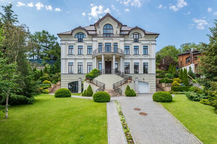 A large, ornate mansion with a sprawling green lawn and a long driveway, symbolizing the wealth of the rich.