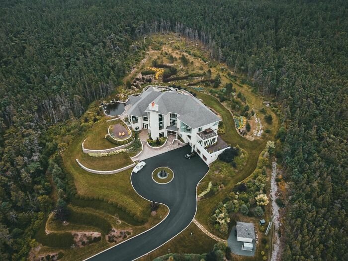 An aerial view of an enormous modern mansion nestled in a forest, representing the extravagant homes of the rich.