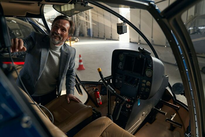 A man smiling while looking out of a helicopter, reflecting the wild moments of working for the rich.
