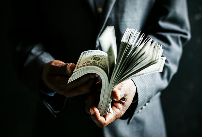 Hands holding a large stack of hundred-dollar bills, illustrating the wealth and rich lifestyle that left people speechless.