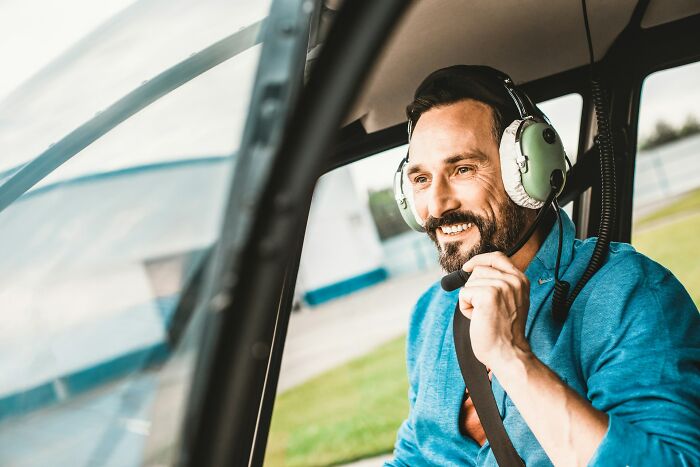 A man in a helicopter headset, smiling, experiencing wild moments from working for the rich.
