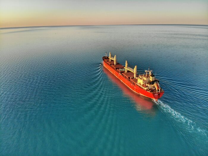 An aerial view of a large red cargo ship sailing on a calm, turquoise sea, illustrating wild moments for the rich.