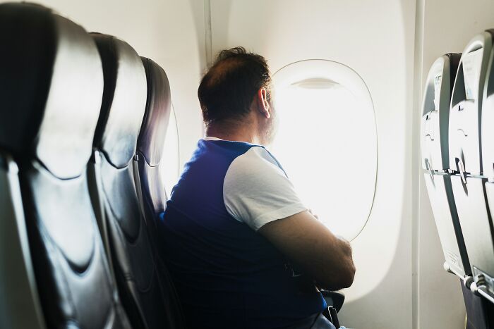 A man sitting on a plane looking out the window, perhaps reflecting on entitled people.