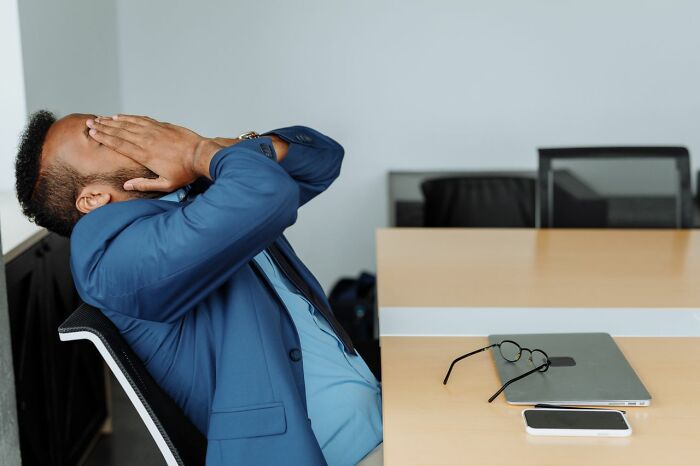 A man in a blue suit covers his face, looking stressed, next to a laptop and phone, depicting the emotional toll of court case stories.