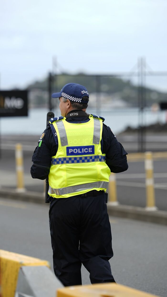 A police officer from behind, wearing a bright yellow vest, potentially handling a difficult court case.