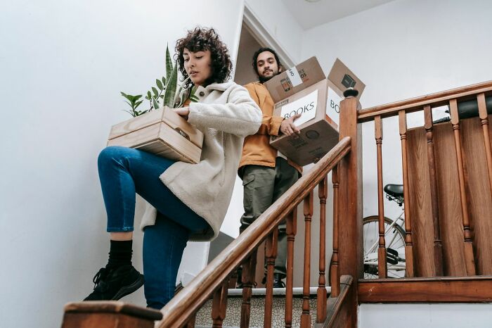 A couple carrying moving boxes and a plant up a staircase, symbolizing a court case related to property.