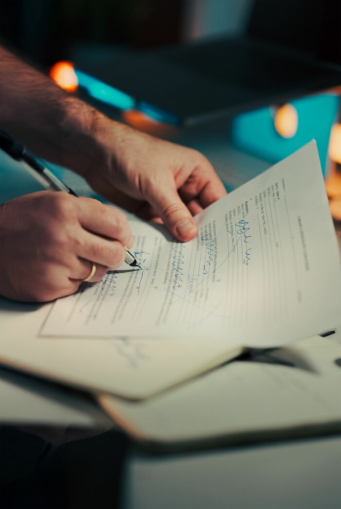A close-up of hands signing a document, representing legal agreements and court case stories.