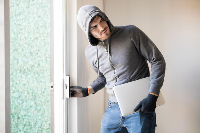 A man in a hoodie carrying a laptop and trying to open a door. This image relates to a court case story about theft.