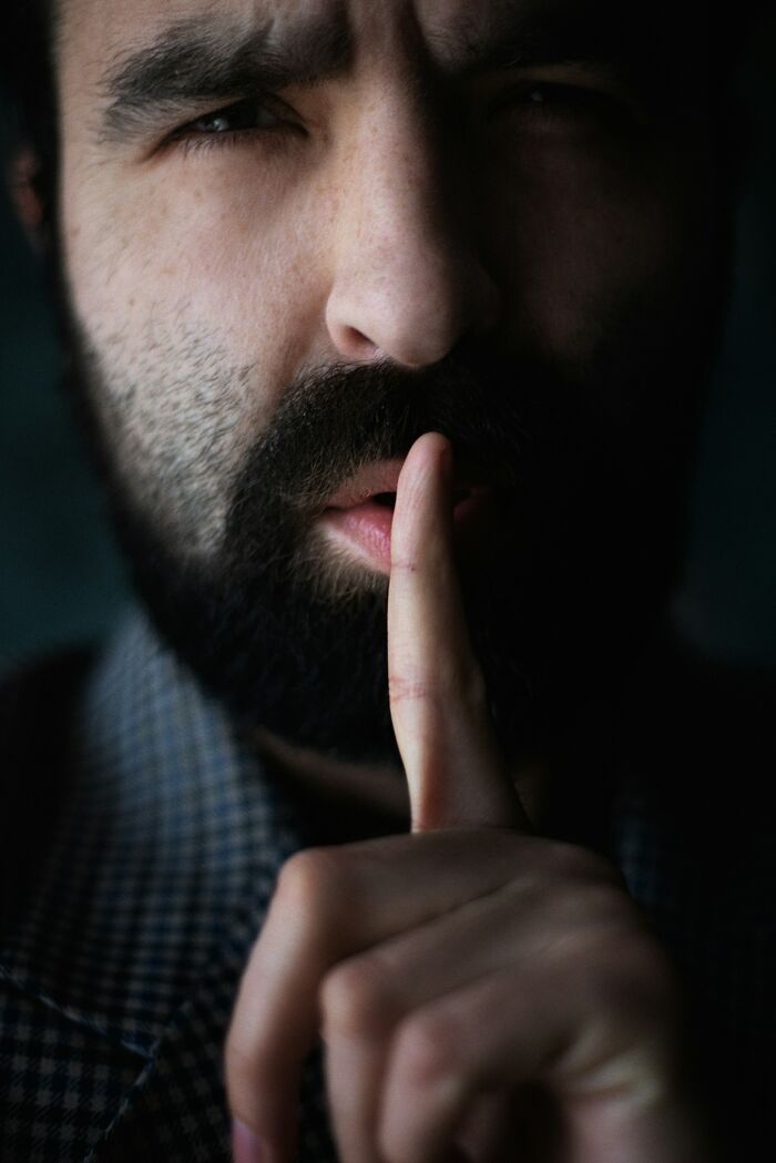 Man with a beard holding a finger to his lips, indicating silence during court case stories.