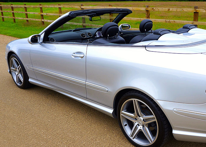A shiny silver convertible car, a symbol of midlife crises, parked on a gravel path.