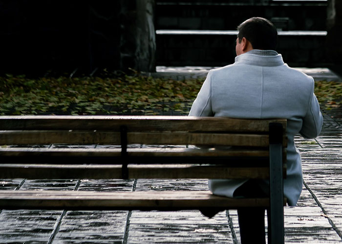 A man sitting alone on a wet park bench, contemplating, a common scene related to midlife crises.