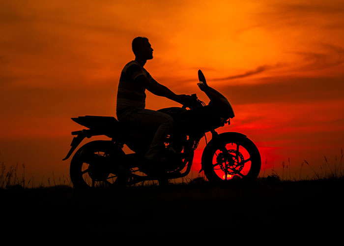 A man silhouetted on a motorcycle against a vibrant sunset, symbolizing a freedom often sought during a midlife crisis.