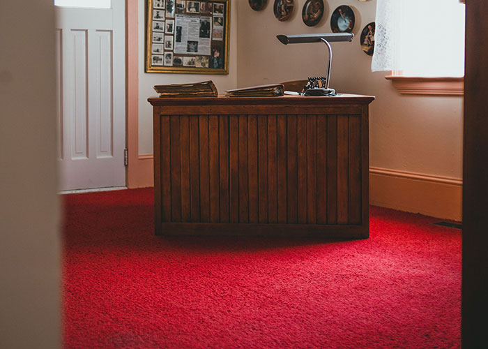 A vintage office desk with a lamp on a bright red carpet, potentially reflecting a midlife crisis with old decor.