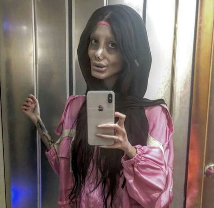 Iranian woman, posing as the Zombie Angelina Jolie, taking a mirror selfie, revealing the illusion of her appearance.