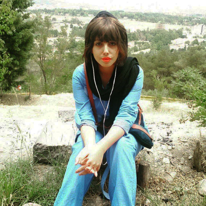 The Iranian woman, known for the Zombie Angelina Jolie illusion, sitting outdoors with orange lipstick.