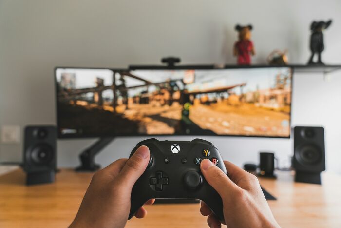 Hands holding an Xbox controller, playing a video game on a monitor. One of the interesting neighbors engaged in a hobby.