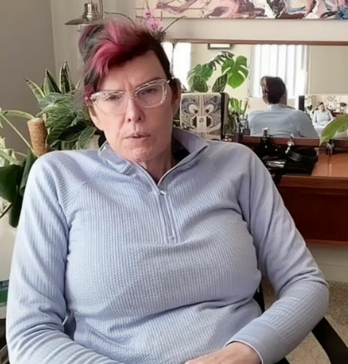 A Trans American recounts horrors after fleeing US for European asylum center, sitting indoors, looking serious. A Trans American recounts horrors after fleeing US for European asylum center, sitting indoors, looking serious.