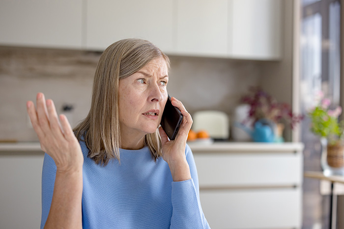 An older woman on the phone, looking upset or angry, making a hand gesture, a MIL image.