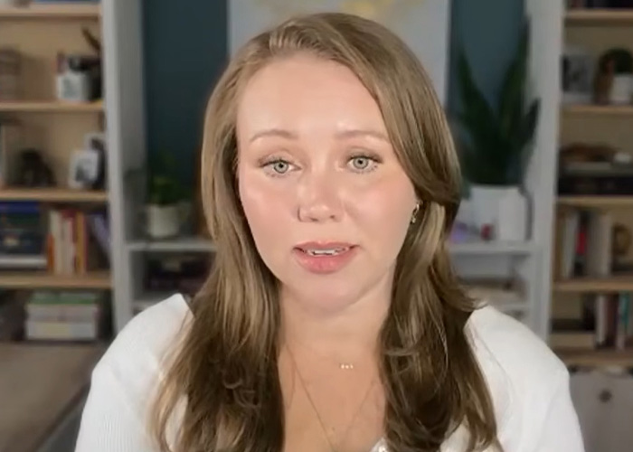 A woman with long hair and a white top speaks to the camera. She escaped a serial criminal and shares the warning sign she ignored.