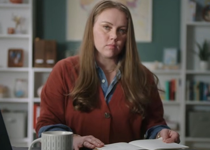 A woman who escaped a serial criminal shares her warning sign. She sits at a desk, looking directly at the camera.