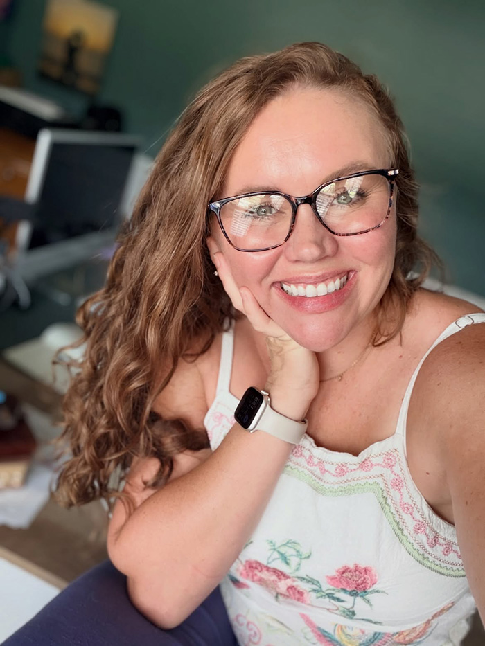 A smiling woman, who escaped a serial criminal, wearing glasses and a floral top, looking happily at the camera.