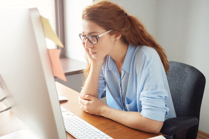A woman at her desk, looking intently at her computer screen, experiencing PTSD mode due to coworkers personal details.