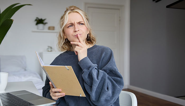 A thoughtful woman holding a notebook, pondering her coworker's actions after giving him her number for tech help.