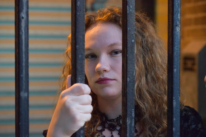 A young woman with curly red hair looks through metal bars, symbolizing being banned from wedding. A young woman with curly red hair looks through metal bars, symbolizing being banned from wedding.